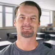 Travis Lancaster Smiling man with brown hair and a graying mustache and goatee